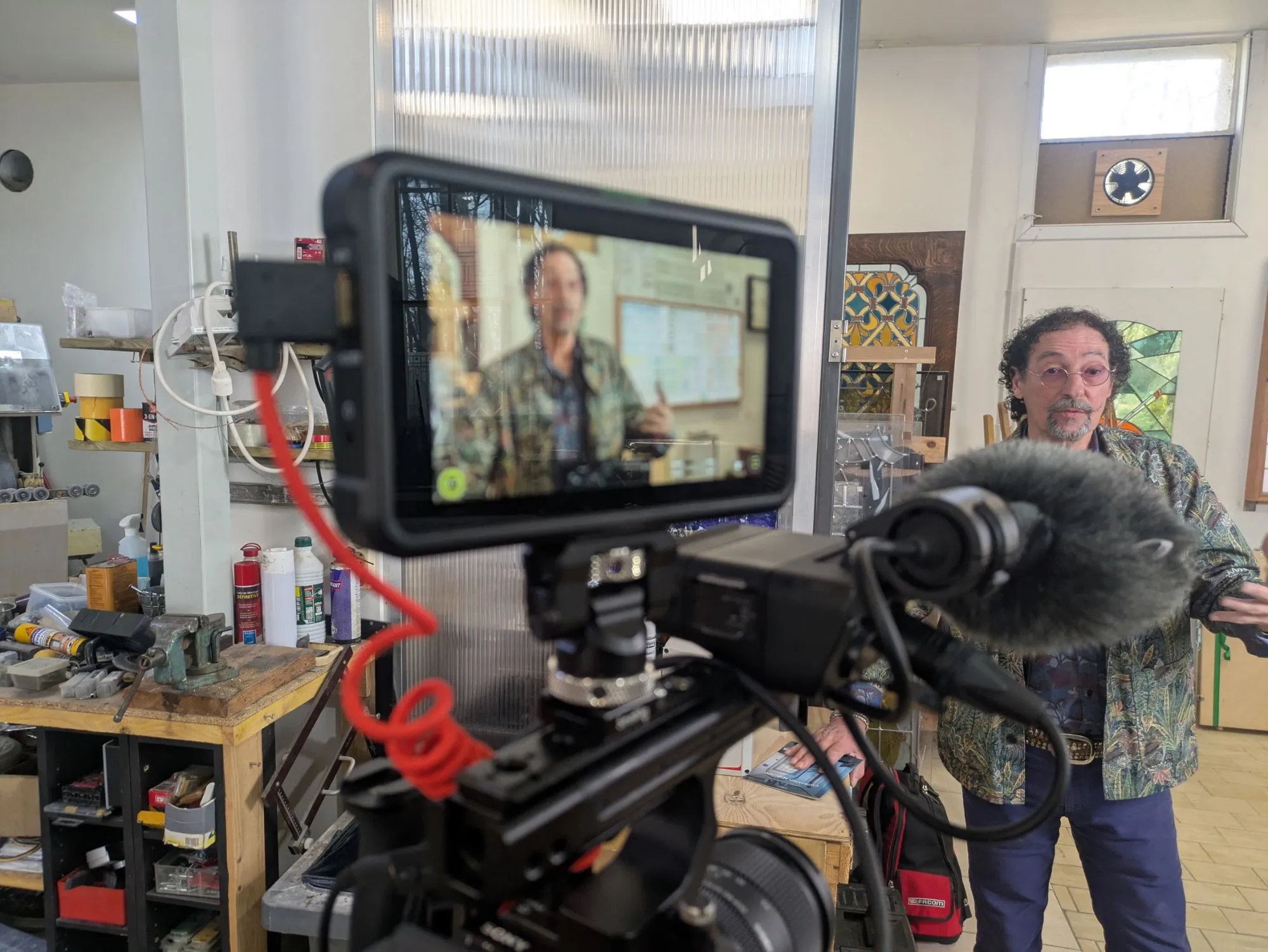 Interview d’un maître verrier dans son atelier, micro et moniteur au premier plan.