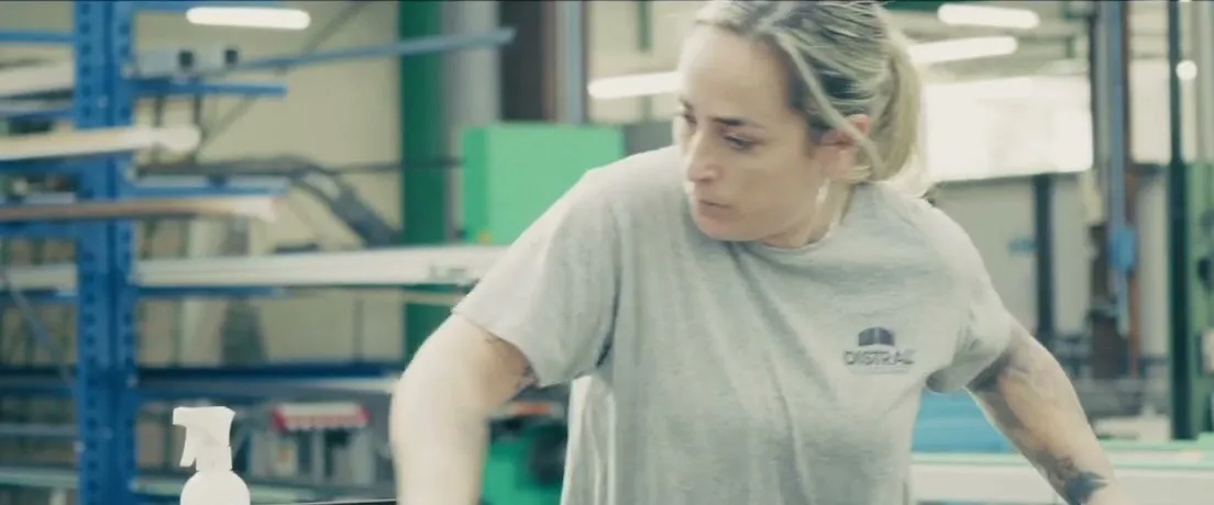 Une opératrice de l’atelier DISTRAL au travail, devant les racks de profilés aluminium.