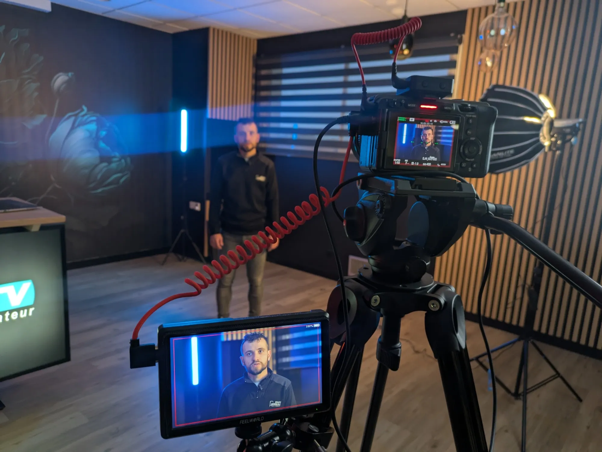 Interview en studio : caméra et moniteur de contrôle cadrent un intervenant éclairé en bleu.