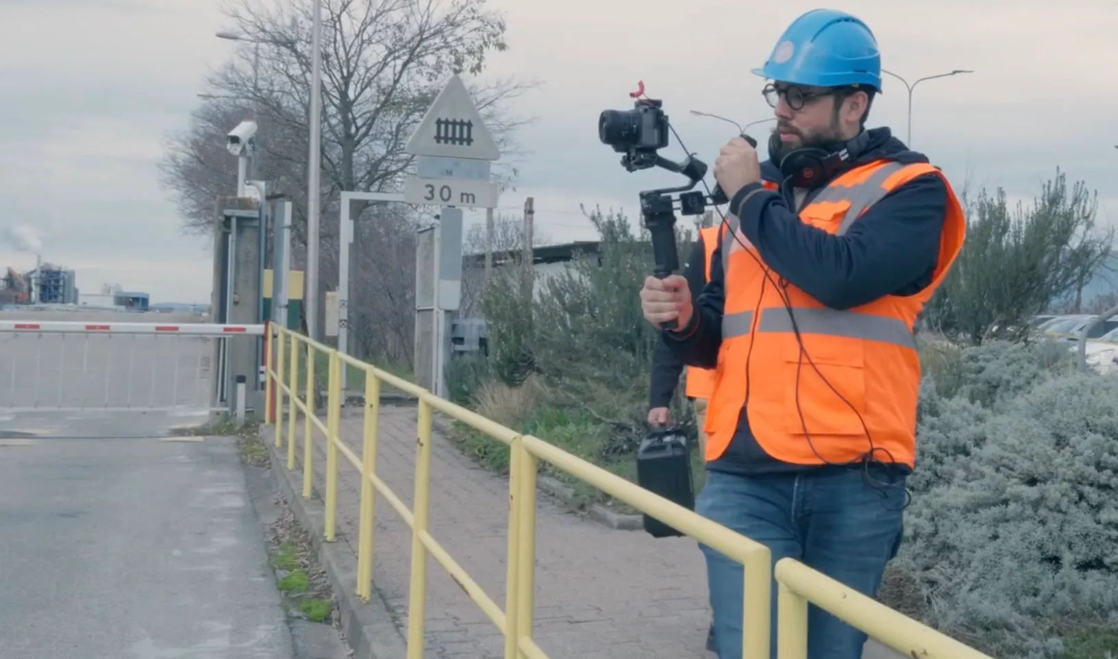 Un cadreur Craftvision en gilet et casque de sécurité filme à la stabilisatrice sur un site industriel.